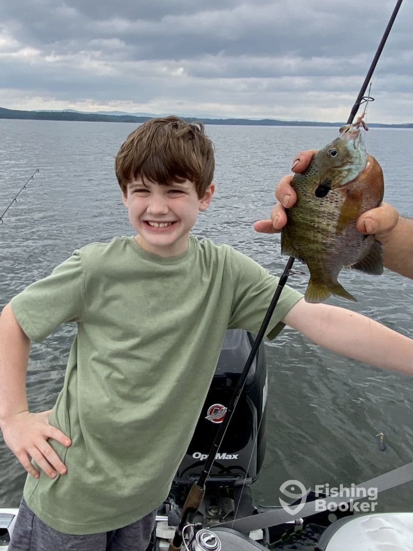 A young angler proudly displaying a Bluegill while fishing on a calm lake, showcasing a joyful moment on the water.