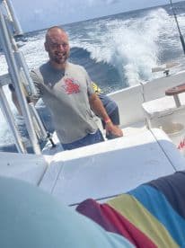 A smiling angler at the helm of a fishing boat, enjoying a day on the open water with friends.
