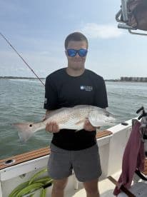 Young angler proudly holding a large Redfish while on a boat, showcasing a successful fishing trip.