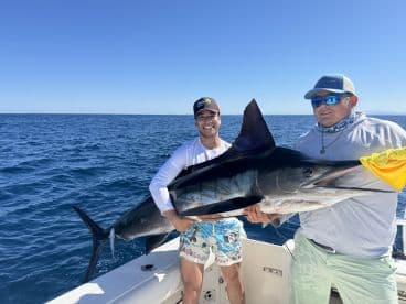 Two anglers proudly displaying a large Marlin on a fishing boat in open waters, showcasing a successful deep-sea fishing trip.