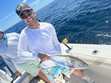 A smiling angler proudly displays a Yellowfin Tuna while fishing on a sunny day in open waters.