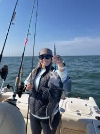 An angler proudly displaying a large Black Sea Bass while fishing on a boat in open waters.