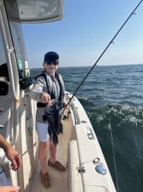 A young angler proudly displaying a Black Sea Bass while fishing on a boat in open waters.