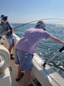 A young angler and an adult are actively fishing on a boat, with the child focused on reeling in a catch while the adult assists, showcasing a dynamic fishing experience.