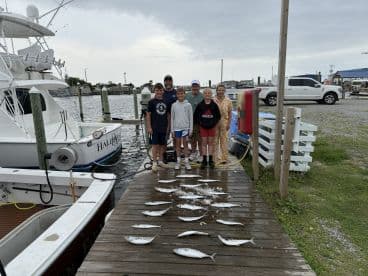 A group of young anglers proudly posing with their catch of fish on the dock, showcasing a successful fishing trip.