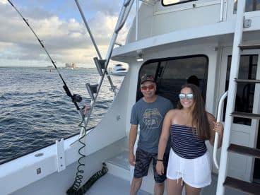 Two anglers enjoying their time on a charter boat, with a scenic view of the water and nearby buildings in the background.