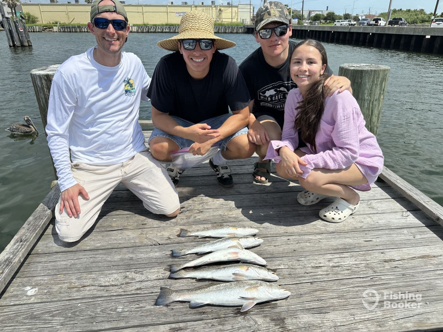 A group of four anglers proudly displaying their catch of Speckled Trout on a dock after a successful fishing trip.
