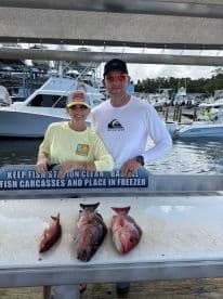 Two anglers proudly displaying their catch of three Snapper species on a cleaning table at a marina.