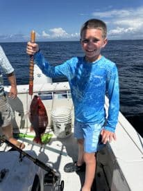 A young angler proudly displaying a Red Snapper on a fishing boat, enjoying a sunny day on the water.