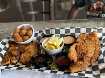 A platter of fried fish and hushpuppies served with sauces and lemon wedges, enjoyed at a casual dining setting.