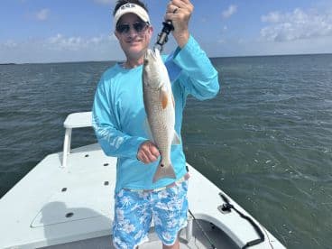 An angler proudly displaying a Redfish while fishing on a boat in a coastal waterway.