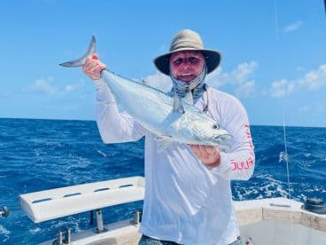 Angler proudly displaying a large King Mackerel while fishing offshore, showcasing a sunny day on the water.