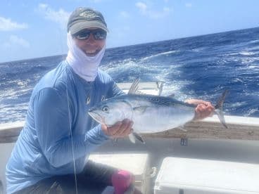 An angler proudly displaying a large Tuna while aboard a fishing boat in open waters.