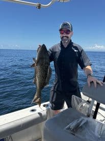 Angler proudly displaying a large Grouper while fishing on a sunny day in open waters.