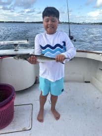 A young angler proudly displaying a caught fish while aboard a fishing boat, enjoying a day on the water.