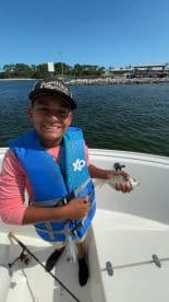 A young angler proudly displaying a small fish while fishing on a boat, showcasing a sunny day on the water.