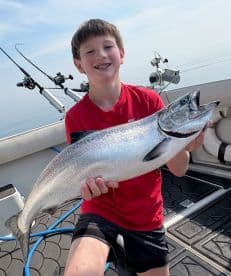 A young angler proudly displaying a large Salmon while fishing on a boat, showcasing a successful day on the water.