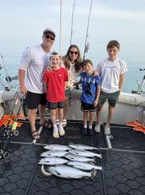 A family of five proudly displays their catch of several trout on the deck of the boat during a fishing charter.