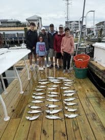 A family group proudly displays their catch of multiple fish on a dock after a successful fishing trip.