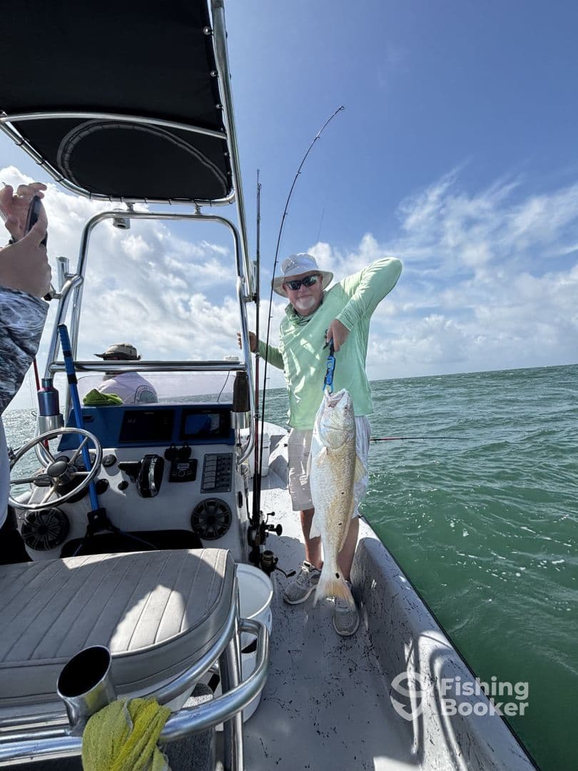 An angler proudly displaying a large fish aboard a boat in a sunny fishing environment.