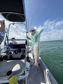 An angler proudly displaying a large fish aboard a boat in a sunny fishing environment.