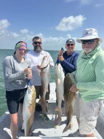 A group of four anglers proudly displaying their catch of Redfish and Speckled Trout on a sunny day in coastal waters.