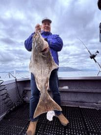 Angler proudly displaying a large Halibut while fishing from a charter boat in open waters.