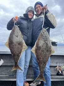 Two anglers proudly displaying their catch of Halibut while fishing in Alaska, showcasing a successful day on the water.
