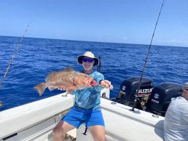 An angler proudly displaying a large Grouper while fishing offshore, showcasing a vibrant blue ocean backdrop.