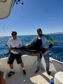 Two anglers proudly displaying a large Marlin on a boat during a deep-sea fishing trip.