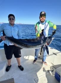 Two anglers proudly displaying a large Marlin on a fishing boat, enjoying a successful day on the water.