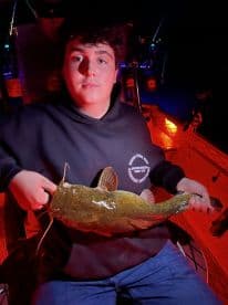 A young angler proudly displaying a large catfish while fishing at night, showcasing the excitement of night fishing.