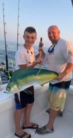 A young angler and an adult proudly displaying a vibrant Mahi Mahi on a fishing boat, showcasing a successful day on the water.