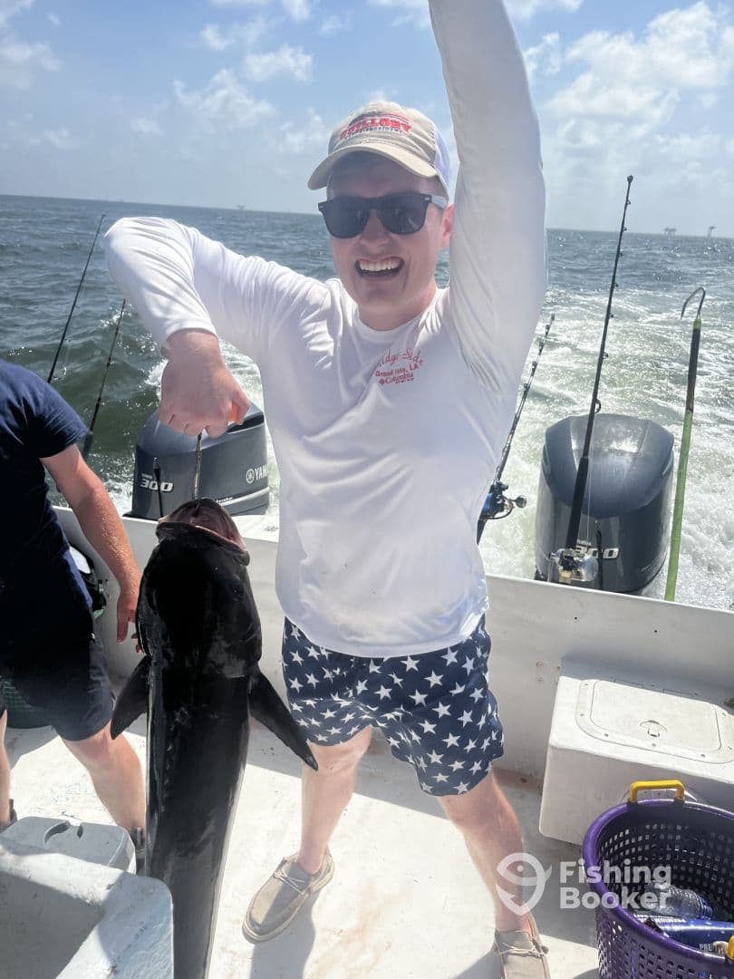 Enthusiastic angler proudly displaying a large fish on a boat during a sunny fishing trip.
