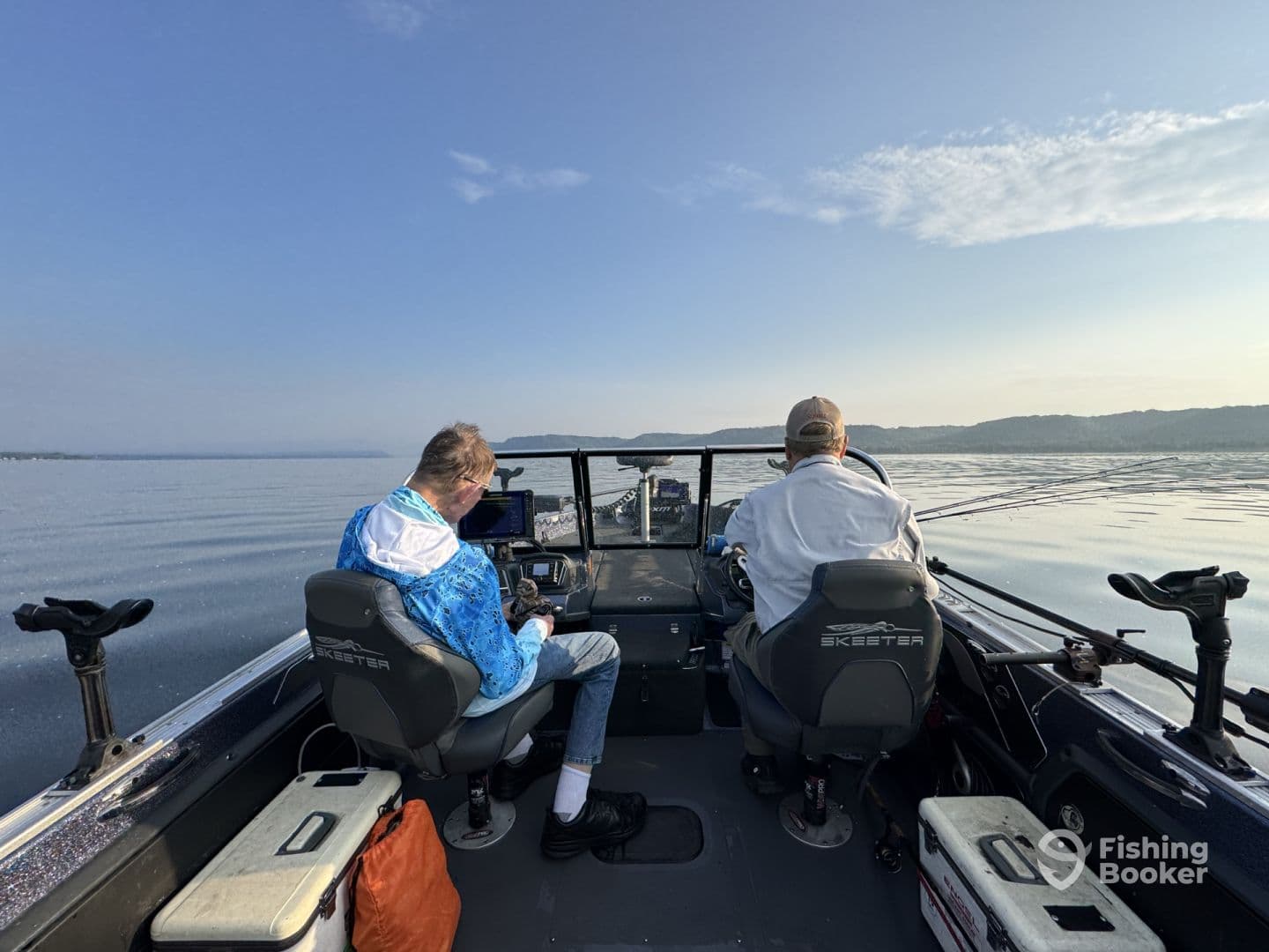 Two anglers seated in a Skeeter boat, navigating calm waters during a fishing trip, showcasing the boat's interior and helm.