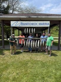 A group of anglers proudly displaying their catch of Salmon at Manitowoc Marina, showcasing a successful fishing trip.