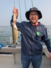 Angler proudly displaying a Walleye caught while fishing on a boat, showcasing a sunny day on the water.