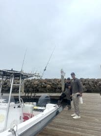 Two anglers posing by a center console boat at the dock, ready for a fishing adventure in overcast weather.