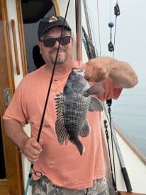 An angler proudly displaying a Black Sea Bass while fishing from a boat, showcasing a successful catch during a coastal fishing trip.