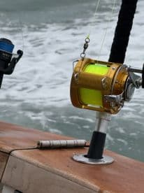 Close-up of a fishing rod and reel setup on a boat, showcasing a bright yellow line and a sturdy rod holder, ideal for deep-sea fishing.