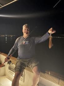 An angler proudly displaying a squid caught during a nighttime fishing trip on a boat.