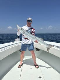 Angler proudly displaying a large Barracuda while fishing offshore, showcasing the excitement of a successful day on the water.