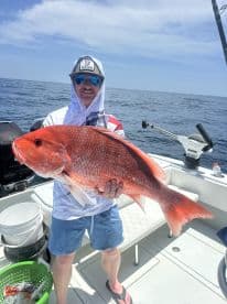 Angler proudly displaying a large Red Snapper on a fishing boat, showcasing a successful day on the water.