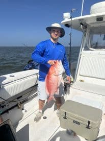 Angler proudly displaying a large Red Snapper aboard a fishing boat in open waters, showcasing a successful day of fishing.