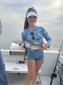 A young woman proudly displaying a caught fish while fishing on a boat, showcasing a beautiful day on the water.