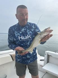 Angler displaying a freshly caught Walleye while fishing from a boat, showcasing the serene water backdrop.