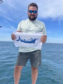 An angler proudly displaying a flag featuring a Marlin while fishing offshore, showcasing the excitement of deep-sea fishing.