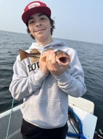Young angler proudly holding a fish while fishing on a boat, showcasing a successful catch in a serene water setting.