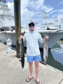 A young angler proudly displaying two large King Mackerel at the marina after a successful fishing trip.