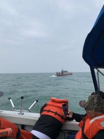 Passengers on a boat wearing life jackets, capturing a passing vessel on a cloudy day at sea.